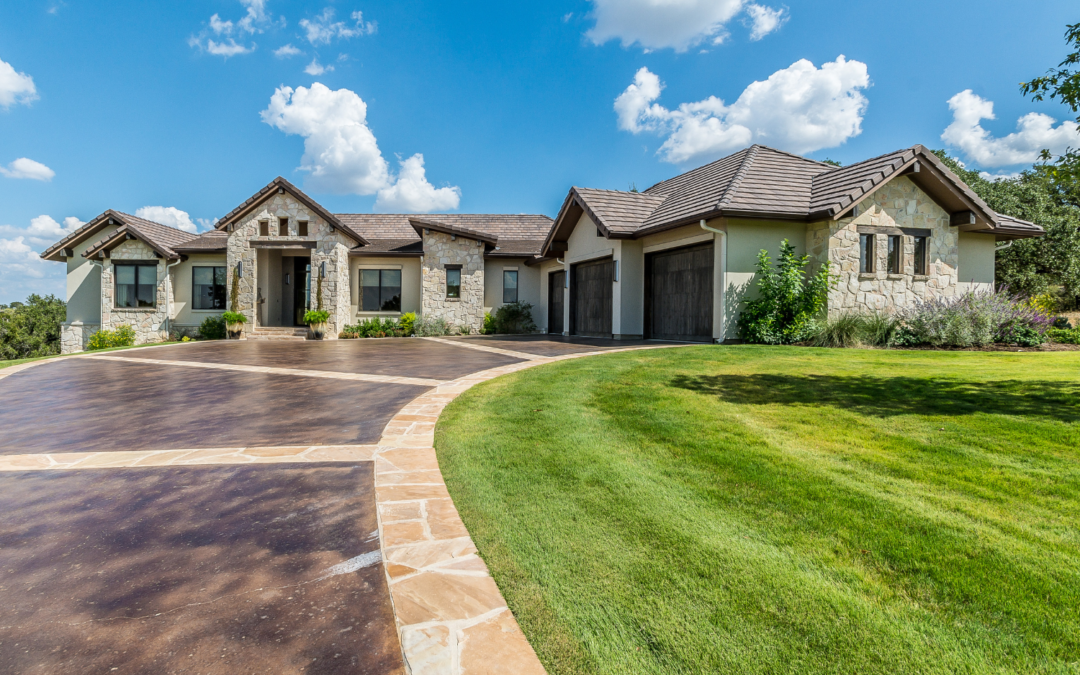 A custom-designed concrete driveway in front of a luxurious stone house with a landscaped yard.